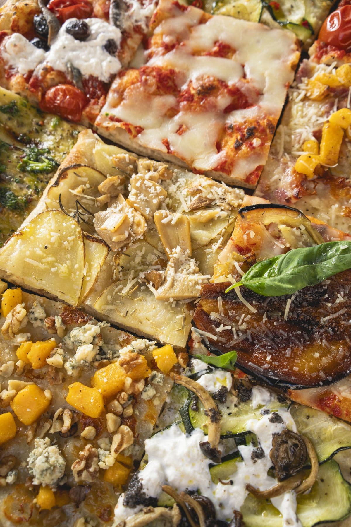 Teglie di pizza al taglio affiancate sul bancone, viste dall'alto
